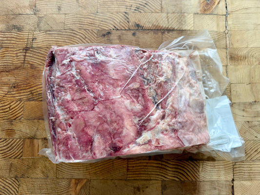 A large frozen cut of meat rib roast, vacuum-sealed in clear plastic and placed on a wooden butcher-block style surface.